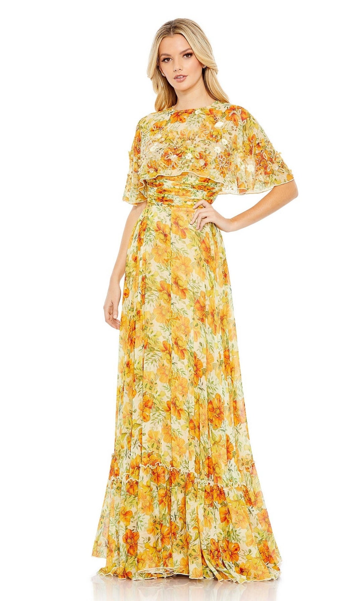 A woman stands with one hand on her hip against a white background, wearing the Long Formal Dress 9201 by Mac Duggal—a yellow floral A-line cape dress with short sleeves and a fitted waist.